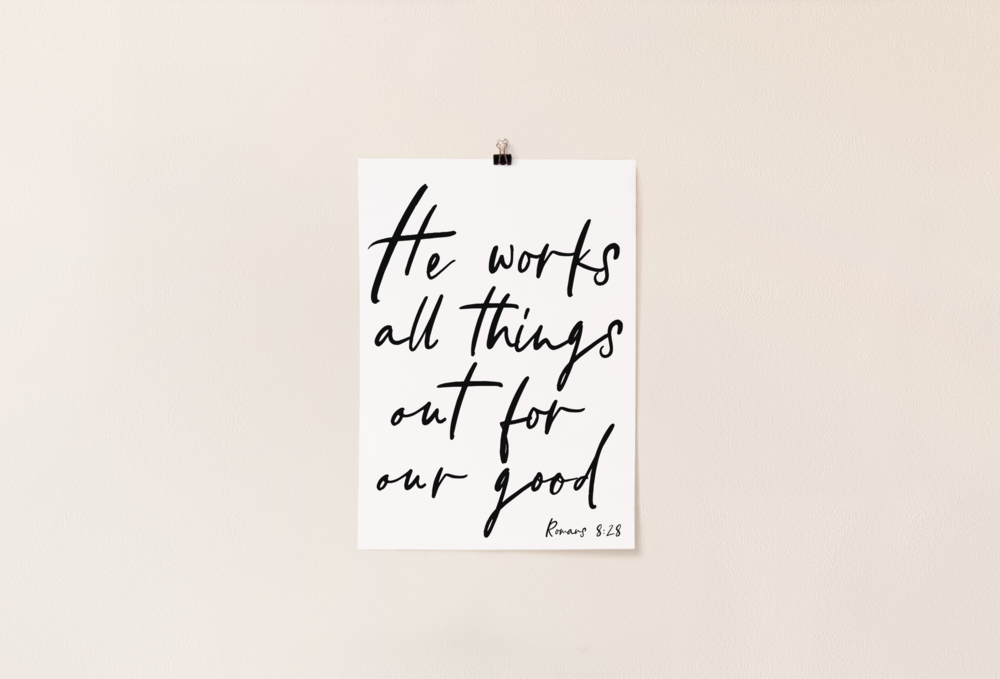 A white poster hanging with the scripture Romans 8:28